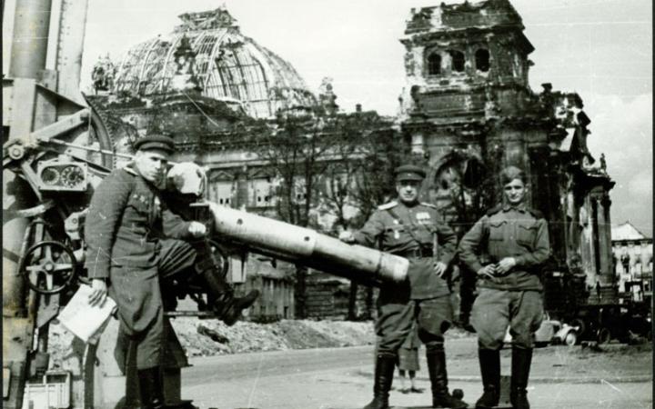 Группа военнослужащих позирует возле разбитого немецкого орудия на фоне поверженного Рейхстага.